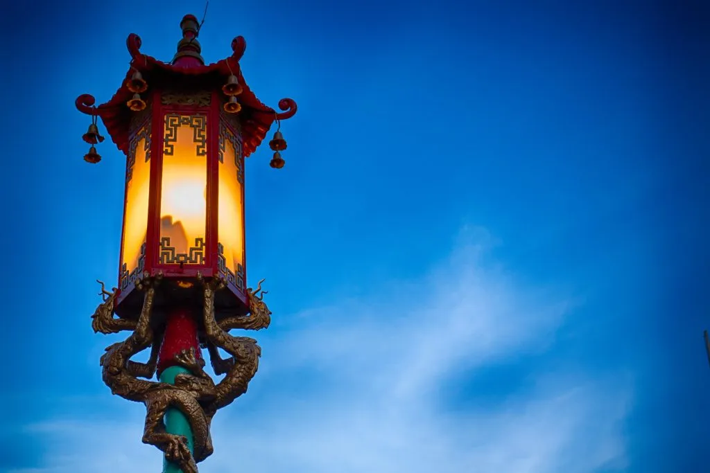A Chinese-style street lamp, illuminated in yellow and red with golden dragon supports, stands out against a deep blue sky